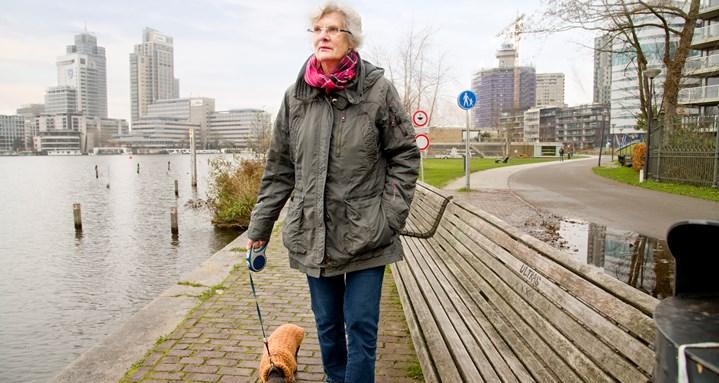 Oudere vrouw laat in de stad hond uit langs de kade 